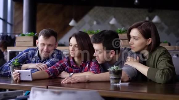 朋友们一起坐在餐厅里使用数字智能手机两个英俊的男人和两个微笑的女人视频的预览图