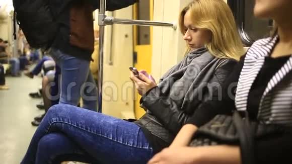 有魅力的女孩在地铁列车上使用智能手机年轻女子用触摸屏技术浏览互联网视频的预览图
