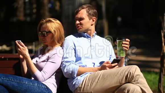 男人和女人朝不同的方向看坐在长凳上所有人都在看他的手机视频的预览图