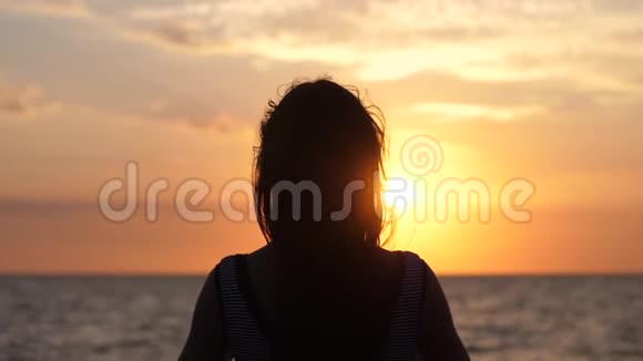 戴耳机的年轻女性剪影在令人惊叹的日落时分在海滩上慢动作地听音乐玩得很开心视频的预览图