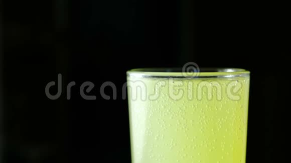 在黑色背景上用碳酸黄色饮料特写半个完整的玻璃视频的预览图