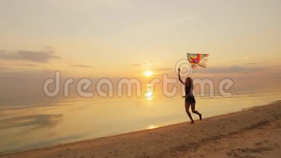 快乐的年轻女人带着风筝跑步日落时分视频的预览图