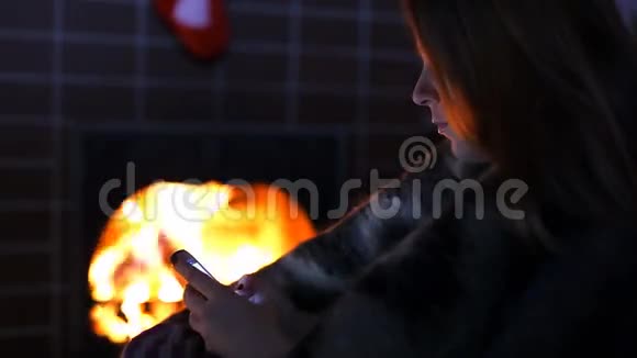 壁炉旁的女孩带着她的智能手机视频的预览图