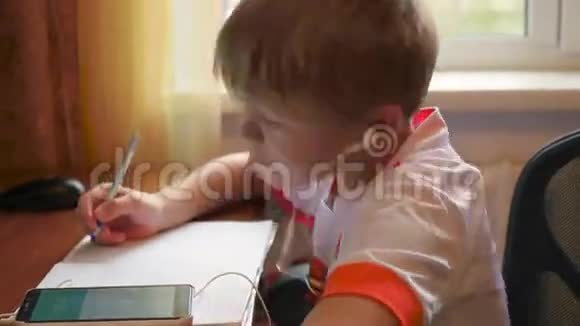 孩子在耳机里听智能手机上的音乐做功课视频的预览图
