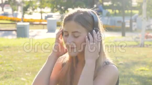 年轻漂亮的女士戴着耳机在户外欣赏音乐视频的预览图