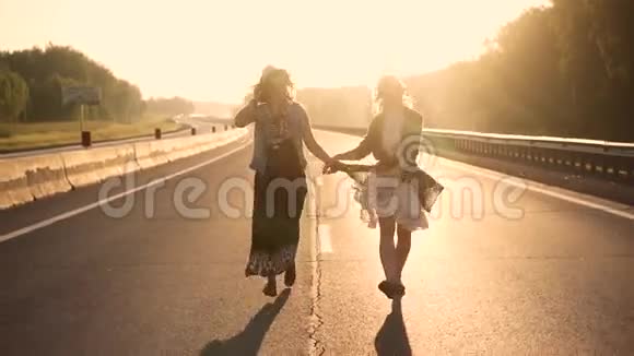 穿着嬉皮士衣服的女孩在一条孤独的道路上奔跑在朝阳的照耀下慢动作视频的预览图