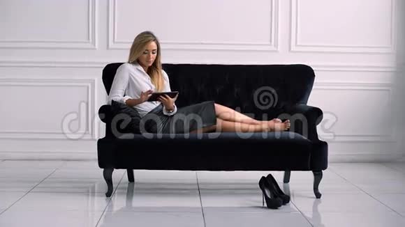 年轻优雅的女商人躺在沙发上用数码平板电脑视频的预览图