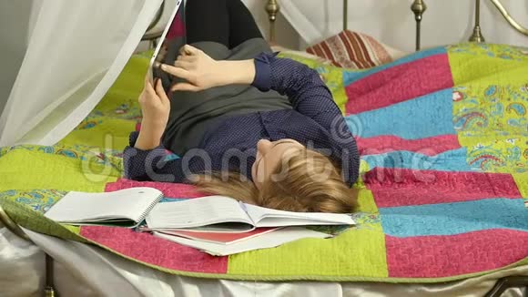 友好的女学生躺在床上看数字平板电脑美丽的女人在家里在线教育慢动作视频的预览图