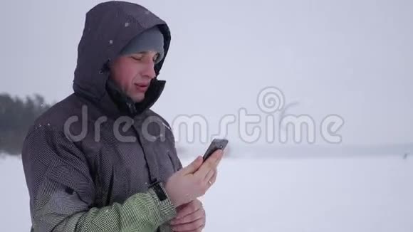 男人自拍选择一个方便的角度在白雪覆盖的湖泊森林和风筝冲浪的背景下4K视频的预览图