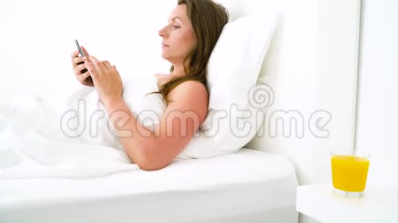 可爱的女人早上检查智能手机在床上喝橙汁视频的预览图