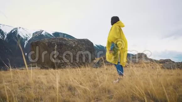 一个穿着黄色斗篷的年轻女孩沿着岩石跑一个旅行者正在山间旅行视频的预览图