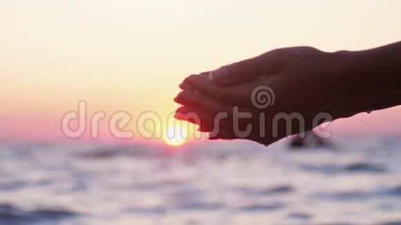在日落时分在海洋背景下雌性的双手在手指间涌出海沙慢动作1920x1080视频的预览图