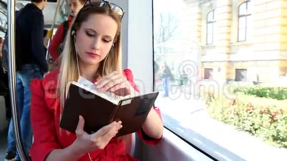 美丽的金发女人坐在电车上看书接电话视频的预览图