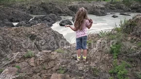小女孩旅行者一个孩子站在山的背景下的山河悬崖边视频的预览图