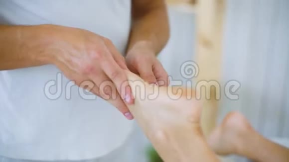 男按摩师在水疗沙龙中按摩双手年轻女性腿脚在桌子上视频的预览图