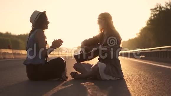 女孩嬉皮唱歌你弹吉他日落时分两个嬉皮士坐在马路上视频的预览图