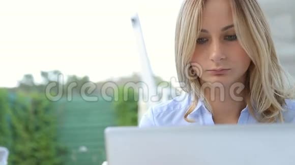 年轻女子用笔记本电脑喝果汁坐在咖啡馆里视频的预览图
