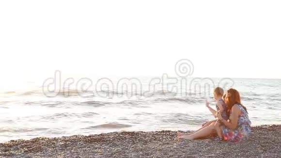 妈妈和两个男孩坐在海滩上儿子在日落时出海视频的预览图