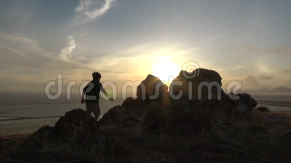 活跃的男孩在日落时爬上大石头视频的预览图