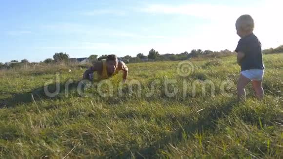 小宝宝站在草地上的青草上看着爸爸做俯卧撑运动员在做俯卧撑视频的预览图