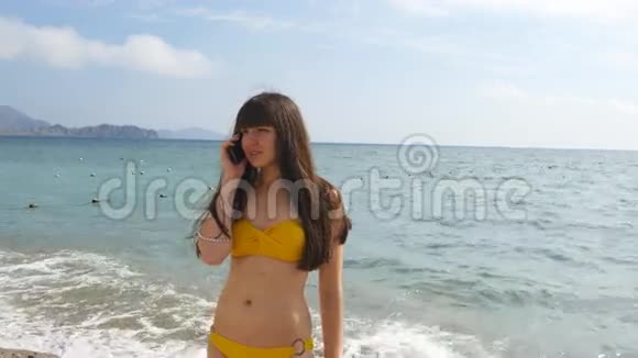 穿着泳衣的年轻迷人的女人正在海边的手机上聊天穿比基尼的严肃女孩在说视频的预览图