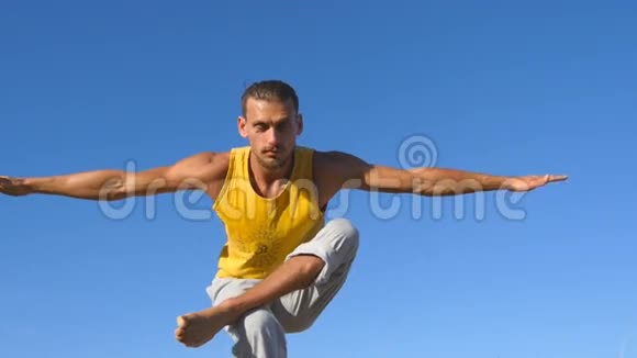 年轻运动男子站在树瑜伽姿势的肖像以蓝天为背景高加索人练习瑜伽动作视频的预览图
