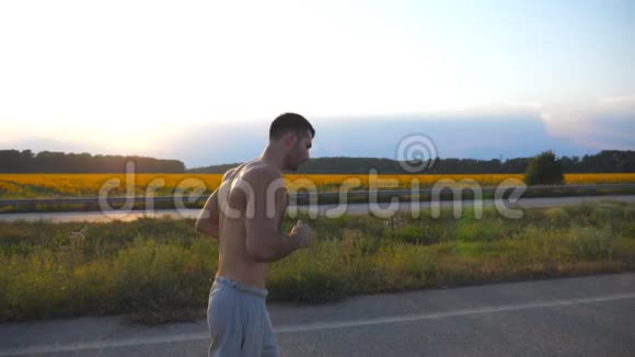 日落时分年轻的肌肉男在乡间小路上慢跑马拉松长跑户外男子慢跑训练概况运动员视频的预览图