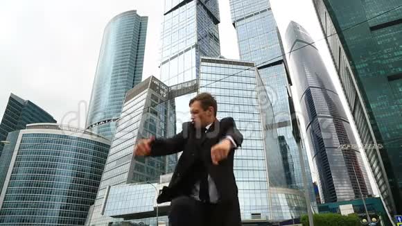快乐的商人在一座商业中心摩天大楼的背景下在一条城市街道上跳舞视频的预览图