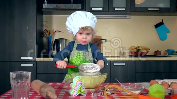 可爱的小女孩在厨房桌子上筛面粉做蛋糕视频的预览图