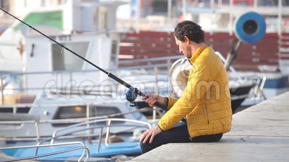 穿黄色夹克的人坐在码头上钓鱼视频的预览图