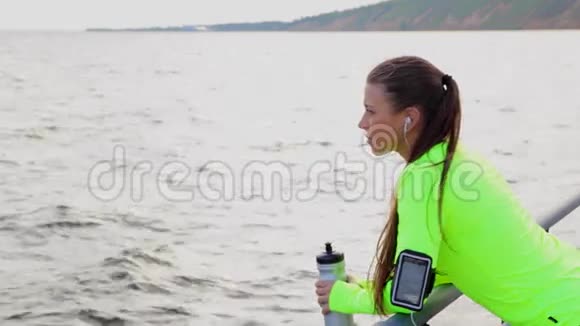 运动女人看海在城市堤上休息喝水视频的预览图