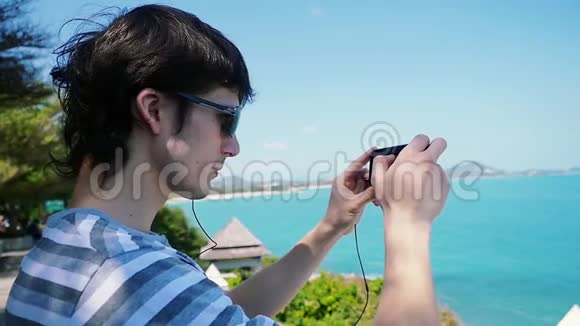 戴太阳镜的年轻人在海滩上用他的智能手机拍照苏梅岛泰国1920x1080视频的预览图