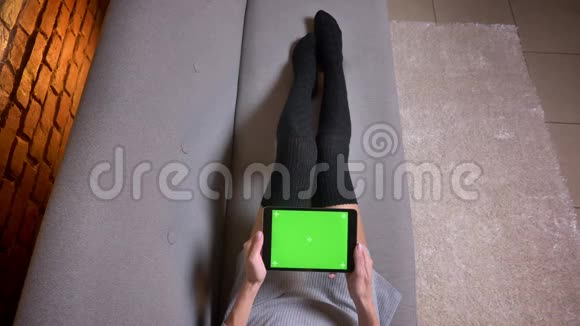 室内沙发上穿着可爱袜子的女腿特写镜头女人拿着绿色屏幕的平板电脑视频的预览图