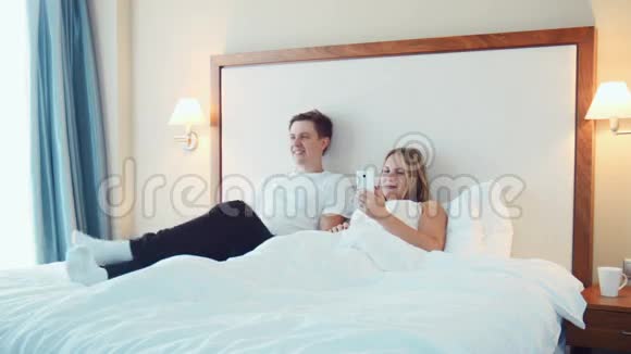 幸福的夫妻躺在床上看电视用智能手机视频的预览图