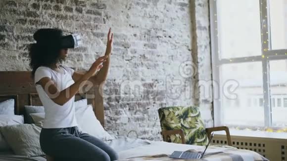 Curly混合种族青少年女孩在家使用虚拟现实360耳机体验视频的预览图