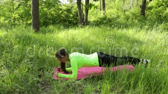 年轻女子在公园的垫子上做木板运动看着镜头微笑视频的预览图