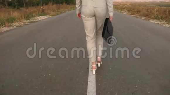 商务女性带着黑色公文包穿着浅色西装穿着白色高跟鞋沿着柏油路走着视频的预览图