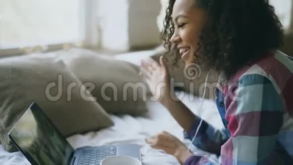 好奇的非裔美国年轻女性躺在床上与朋友视频聊天时聊天视频的预览图