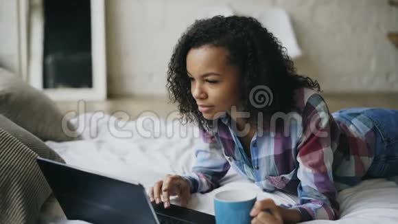 年轻迷人的非洲女孩使用笔记本电脑分享社交媒体躺在家里的床上视频的预览图