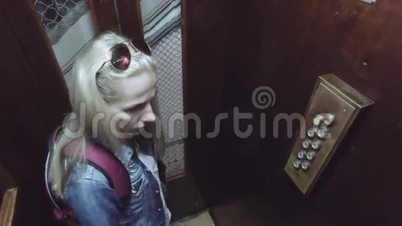 带背包的年轻女子在旧工作笼电梯里按下液位按钮向下移动视频的预览图