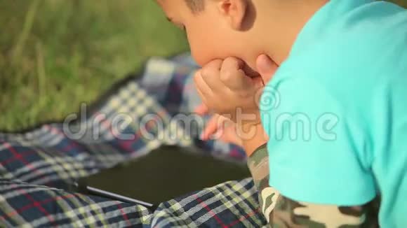 在草坪上玩平板电脑的男孩视频的预览图