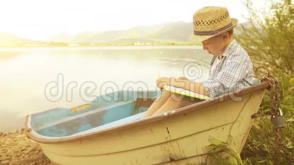 小男孩戴着草帽坐在乡村小船上看书视频的预览图