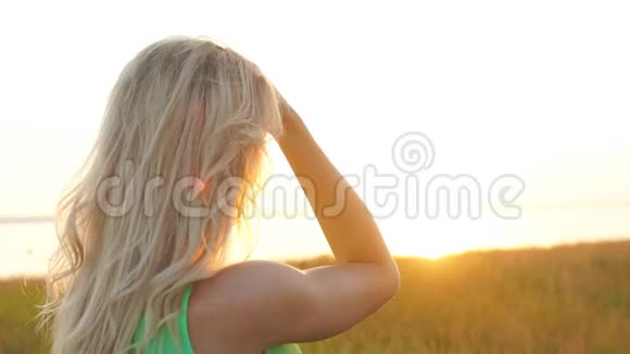 日落时分美丽的金发女郎在田野里散步特写视频的预览图