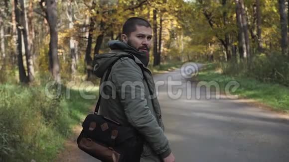 年轻的帅哥穿着夹克走在秋天的森林里关于公园性质的肖像往前走视频的预览图