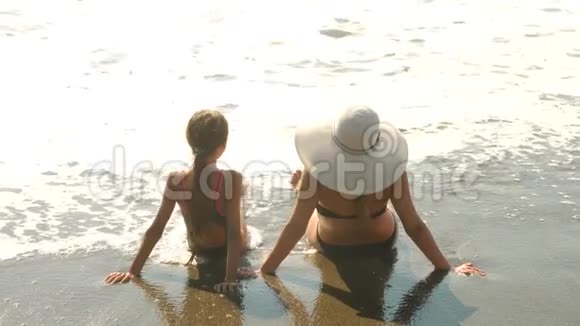 母亲和女儿坐在海边水溅起他们的腿慢动作波浪遮住了腿4k视频的预览图