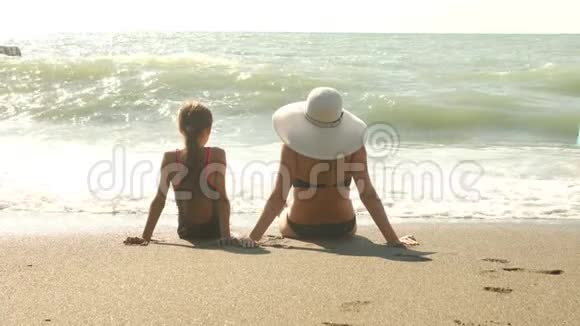 母亲和女儿坐在海边水溅起他们的腿慢动作波浪遮住了腿4k视频的预览图