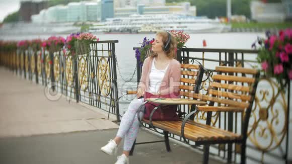 一个女孩用智能手机坐在沙滩上的花凳上听着耳机里的音乐跳舞游艇和视频的预览图
