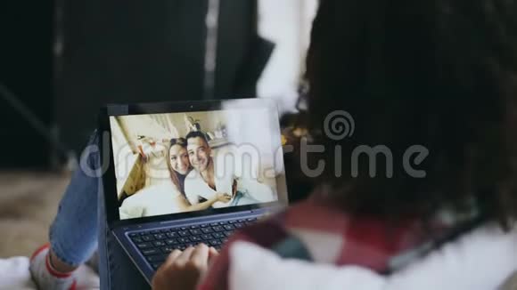 好奇的年轻女性躺在床上和朋友用笔记本电脑聊天视频的预览图