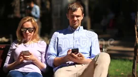 男人和女人朝不同的方向看坐在长凳上所有人都在看他的手机视频的预览图