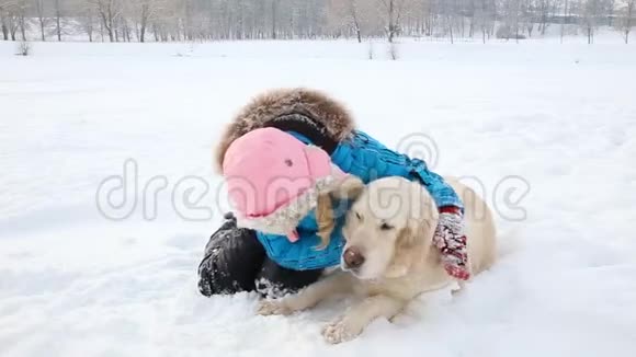对宠物的爱女孩正和一只金色的猎犬在公园的雪地里休息视频的预览图